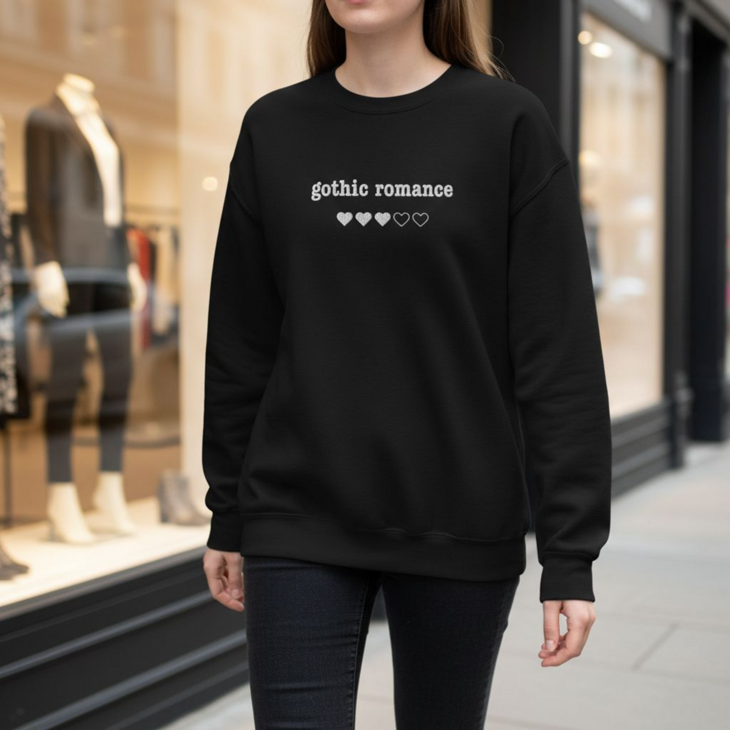 Person wearing a black sweatshirt with 'gothic romance'  embroidered text and heart symbols in an urban setting.
