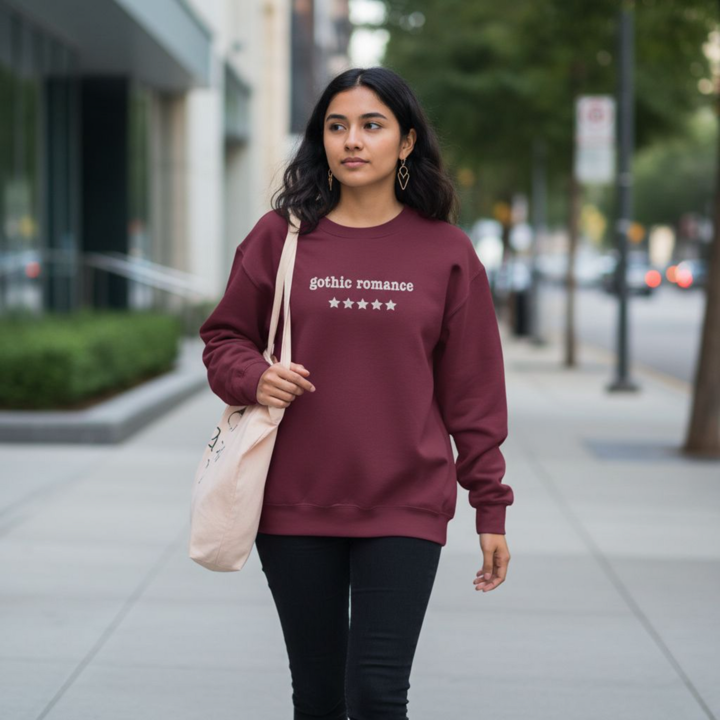 Woman wearing a maroon sweatshirt with gothic romance embroidered text, walking on a sidewalk.